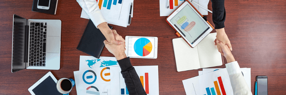 Top-down view of a business team reviewing charts, reports, and laptops together, representing data-informed collaboration and delivery oversight.